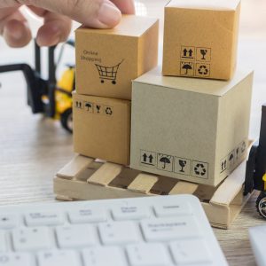 Mini forklift truck load cardboard boxes with symbols on wood pallet and fingers over its and keyboard nearby. Logistics and transportation management ideas and Industry business commercial concept.